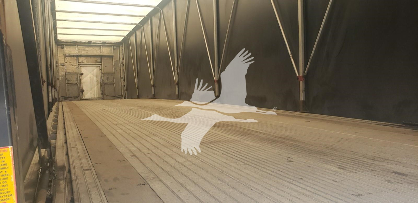 Trailer interior showing empty curtainside trailer with ribbed floor and rear door, branding of a flying bird logo on the floor.