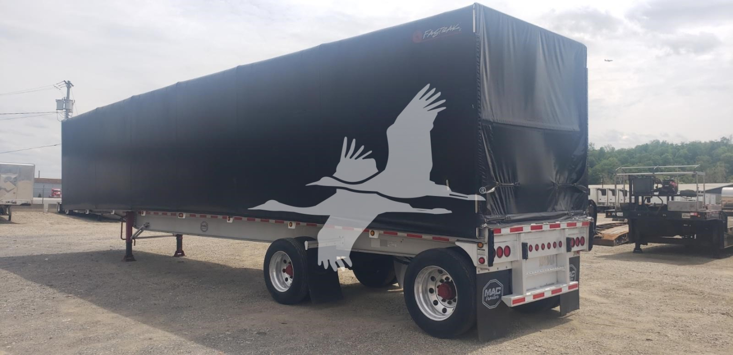 Trailer in a lot with a black tarp cover labeled Mac 72K Beam, curtainside trailer, dual rear axles, white graphic of birds on tarp.
