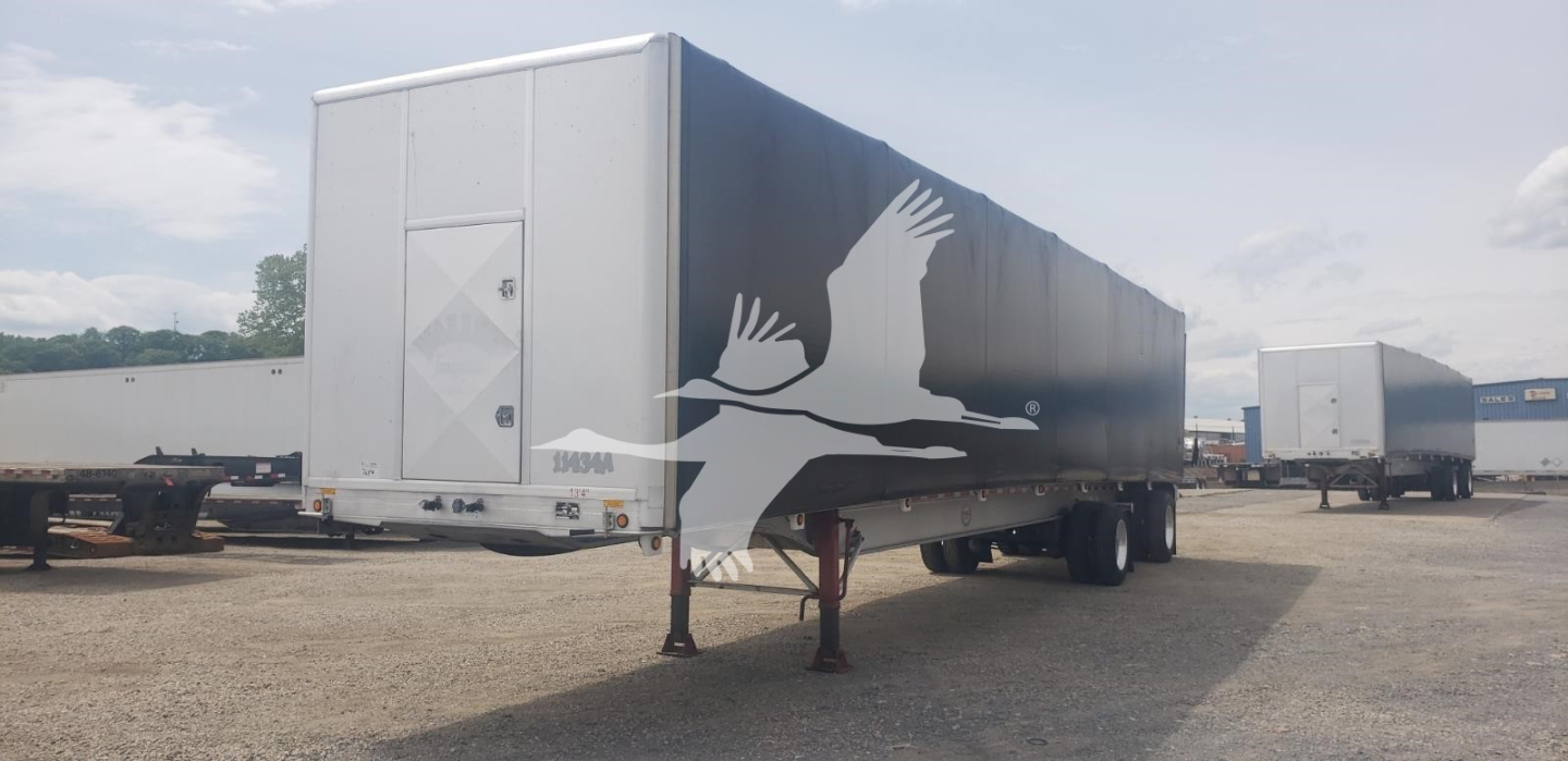 Curtainside trailer in a lot showing the rear end with a raised landing gear and a diamond-shaped access door.
