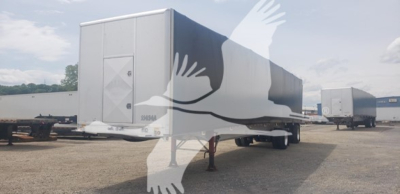 Trailer in a yard showing a curtainside semi-trailer with a closed rear door and side panels, under clear sky.