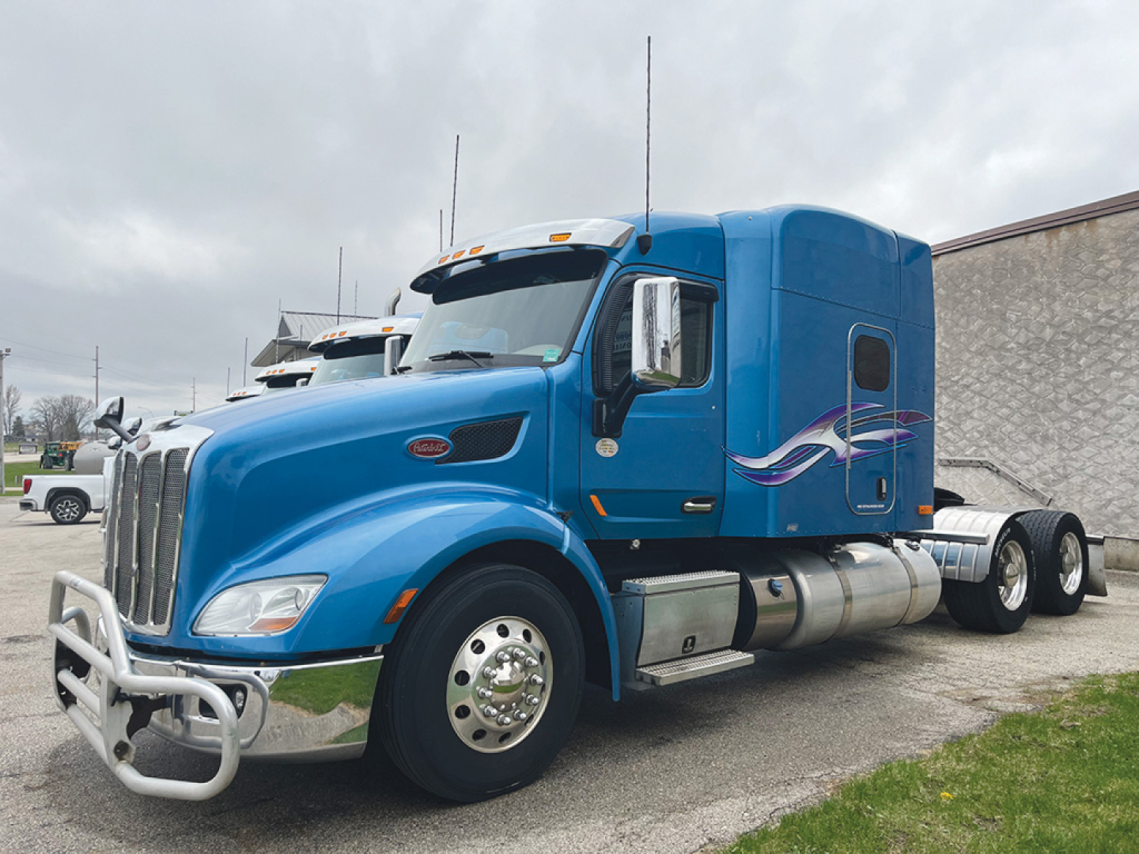 Peterbilt 579 UltraCab tractor side view showing blue exterior with decorative purple white graphics and chrome fuel tanks.