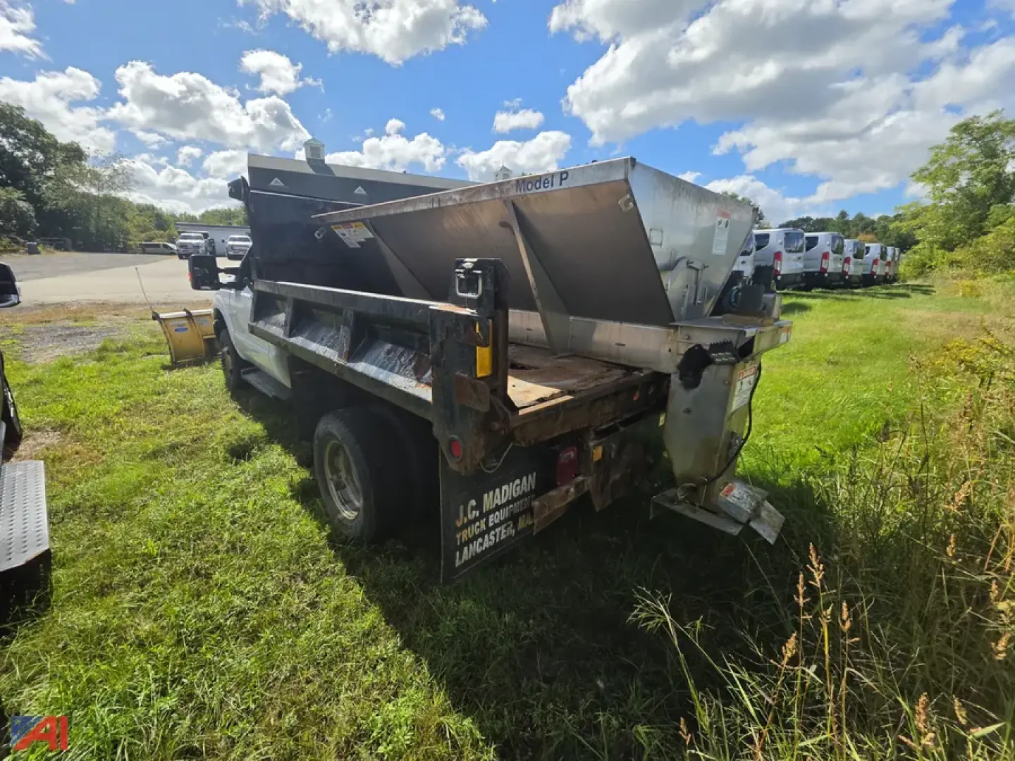 Ford F-350 Super Duty chassis with sander and plow in a field, dual rear wheels, rear view showing metal hopper and truck bed equipment.