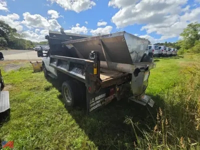 Ford F-350 Super Duty chassis with sander and plow in a field, dual rear wheels, rear view showing metal hopper and truck bed equipment.