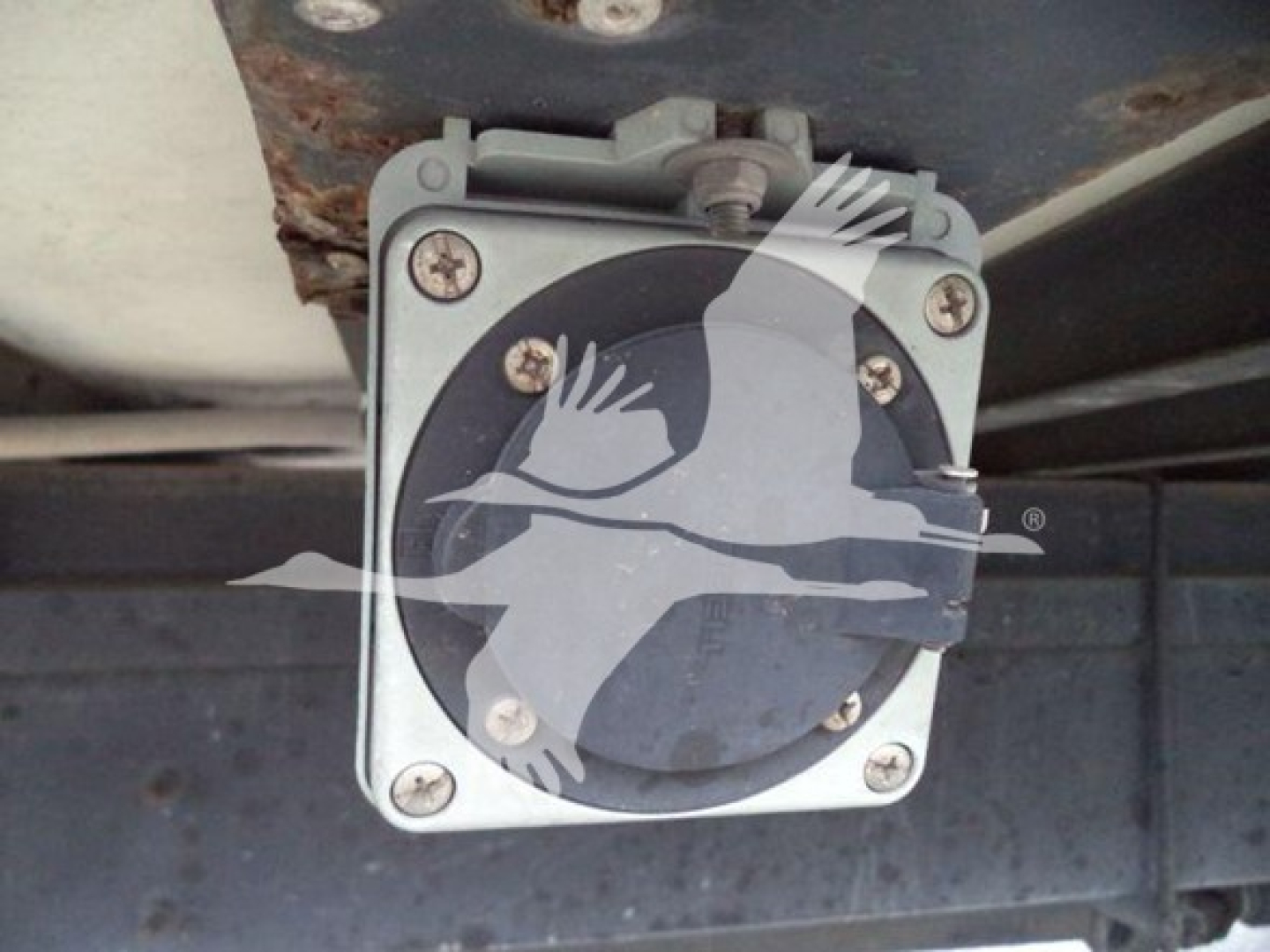 Hino truck engine bay tag or cap visible under chassis with round dial-like component secured by four screws.