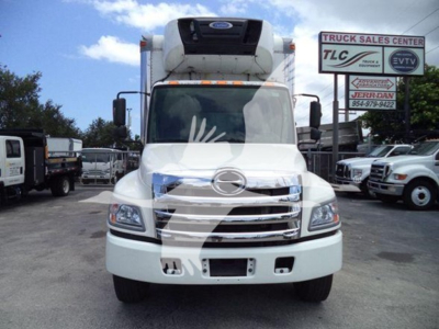 Hino 268a refrigerated truck front view showing grille and cab, white color, with HVAC unit on top and dealership lot in background.