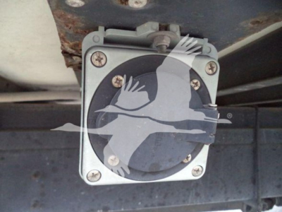 Hino truck engine bay tag or cap visible under chassis with round dial-like component secured by four screws.