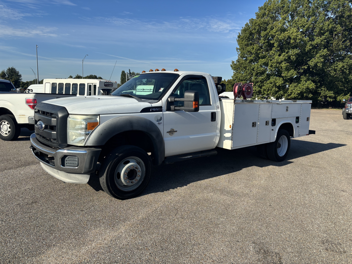 White 2012 Ford F-550 service/utility truck with utility bed and equipment on a sunny day. Side view showing cab, dual rear wheels, and tool compartments. No visible text on body other than standard styling.