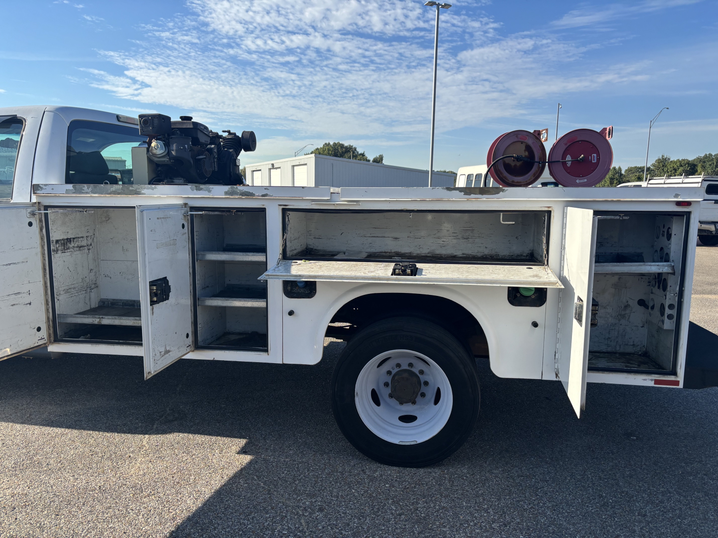 Service/utility truck side storage compartments open showing multiple drawers and shelves with a wheel in foreground and reels in background.