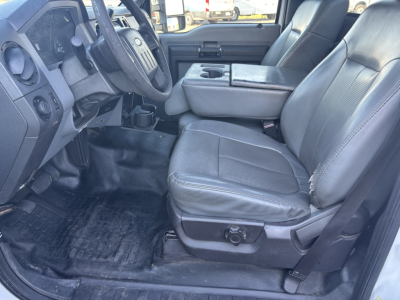 Ford F-550 cab interior showing driver and passenger seats, center console, steering wheel, and dashboard; factory black leather seats with basic controls visible.