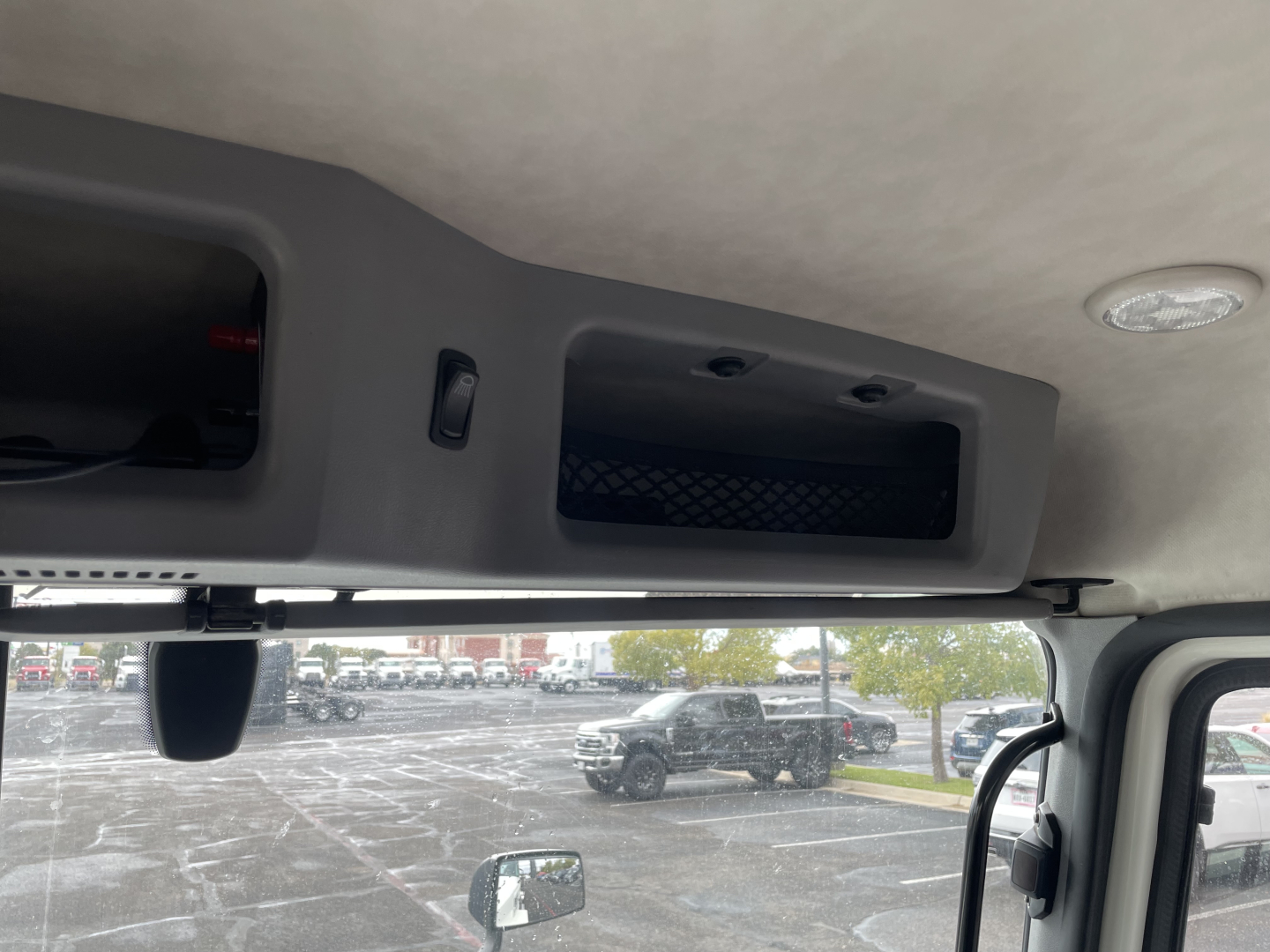 Cargo area view inside a Mack AN64T cab showing overhead compartments and a small vent, with windshield and exterior trucks visible.