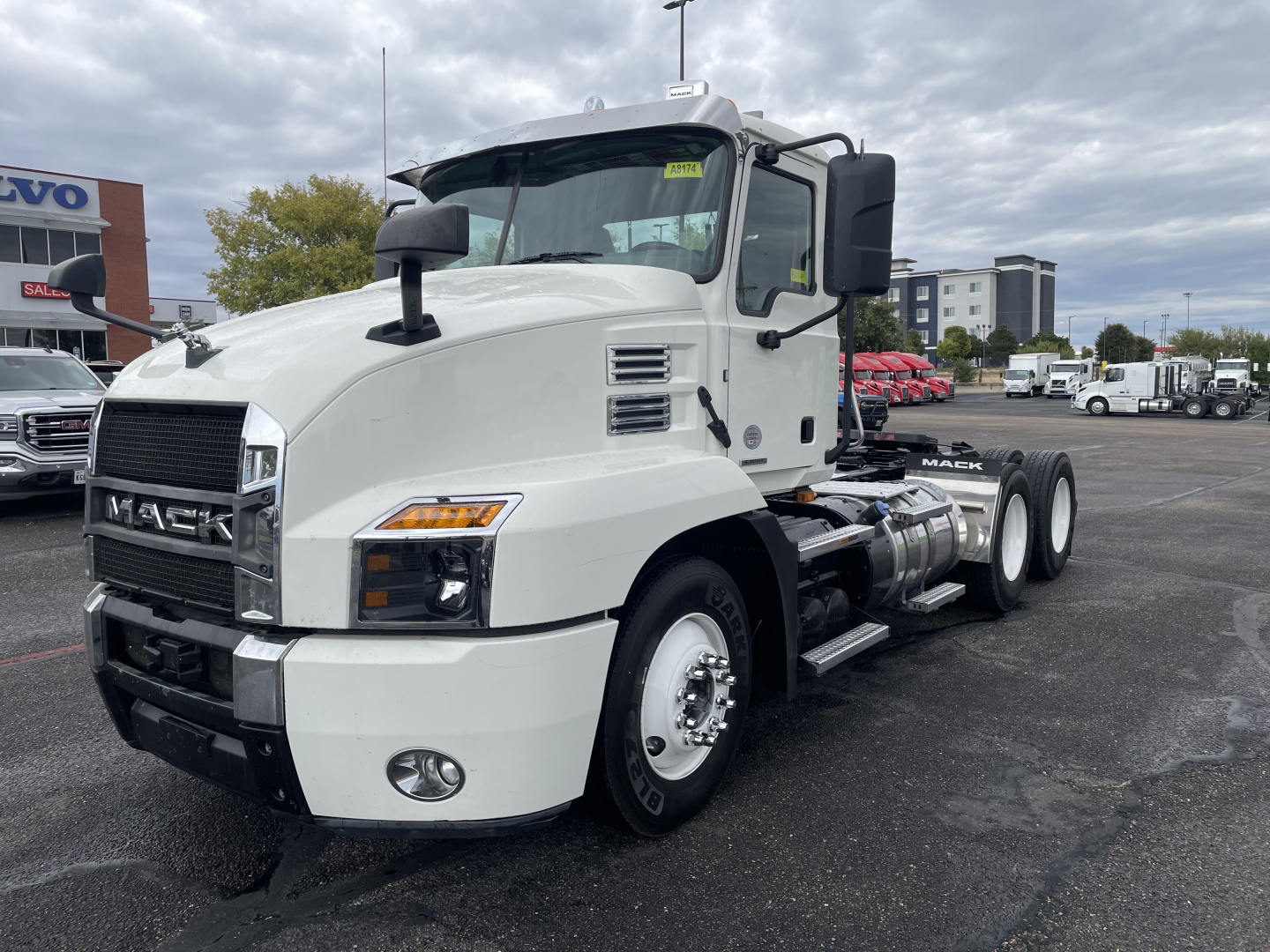 Mack AN64T conventional daycab truck front-left view showing white cab, large grille, dual rear axles, fuel tanks, and side mirrors.