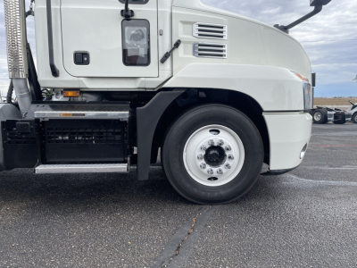 Truck side view showing front wheel and cab of a 2021 Mack AN64T conventional daycab with light gray exterior and black steps.