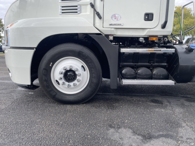 Truck wheel well and side of a 2021 Mack AN64T Daycab showing front wheel with rim, black fuel tanks, steps, and cab exterior; no legible model text visible on image.