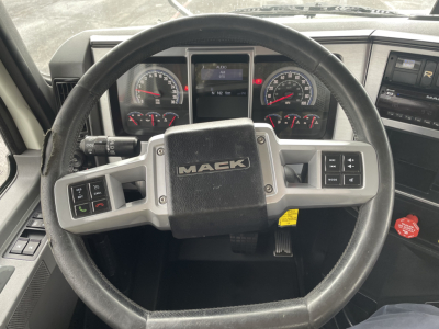 Steering wheel and instrument cluster of a Mack AN64T truck cab, showing the Mack logo on the center pad and dual gauge displays behind the wheel.
