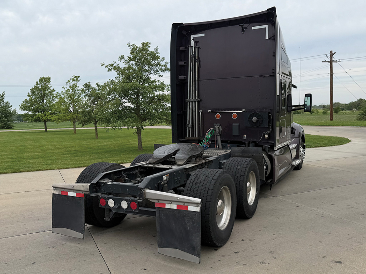 Kenworth T680 tractor rear view showing fifth wheel, dual rear axles, and mud flaps with reflective strips.