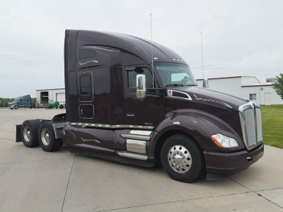 Kenworth T680 with dark purple paint in a parking lot, side view showing sleeper cab and dual rear axles, no visible text on label