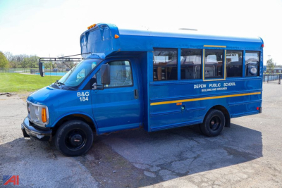 Blue GMC Savana school bus showing B&G 184 on front and Depew Public School text along side, side windows and yellow stripe.