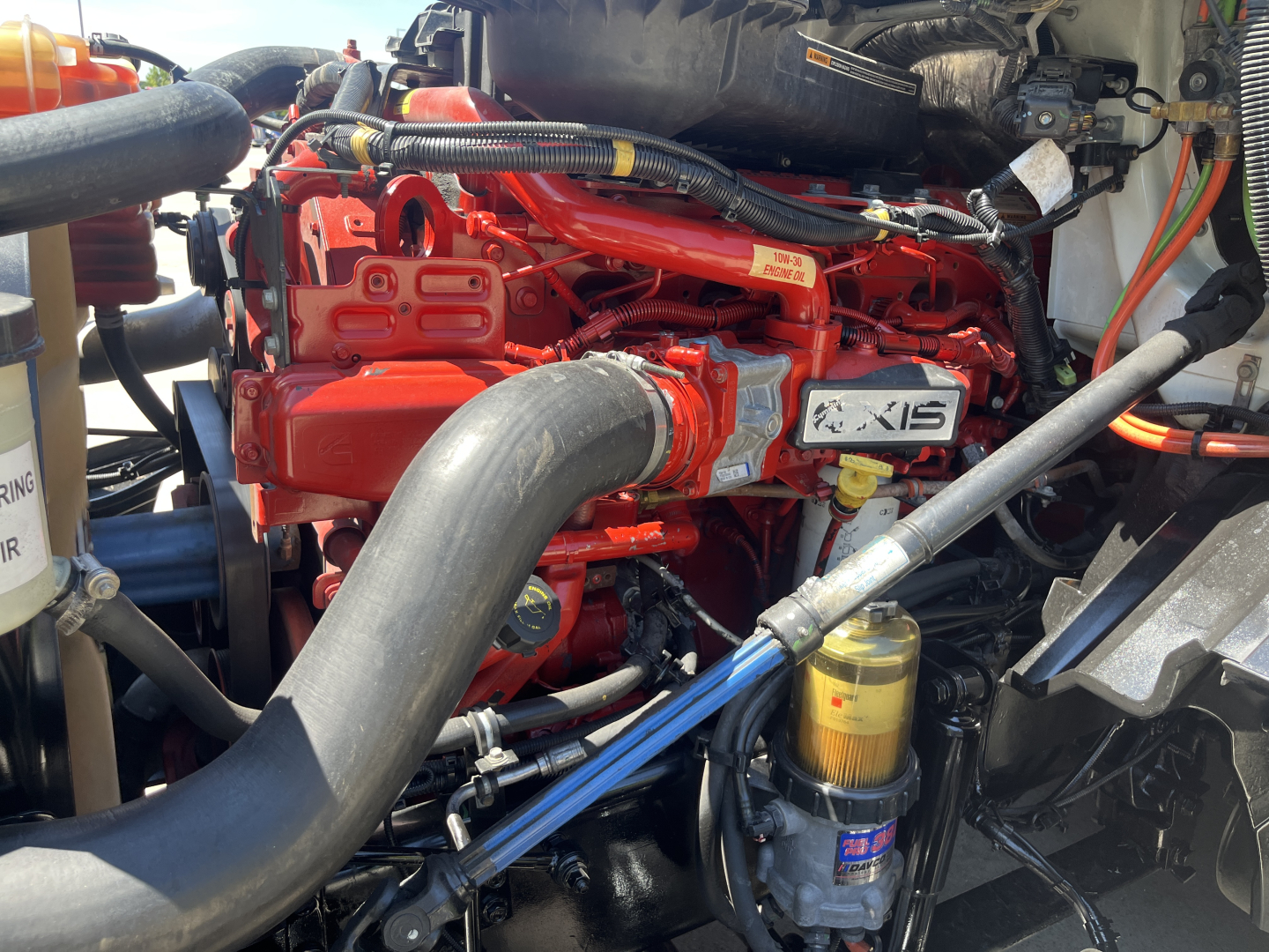 International LT625 engine bay showing red engine block with XIS badge, large black intake hose, yellow oil filter, and various hoses and cables in the engine bay.