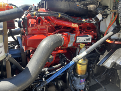 International LT625 engine bay showing red engine block with XIS badge, large black intake hose, yellow oil filter, and various hoses and cables in the engine bay.