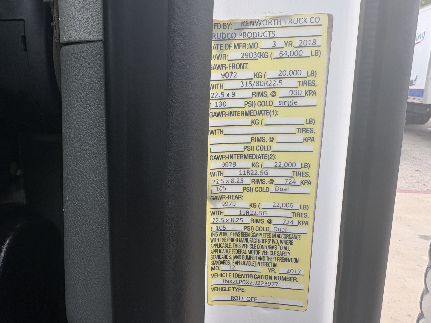 Vehicle identification sticker on Kenworth T880 roll-off truck showing axle weights and tires specifications.