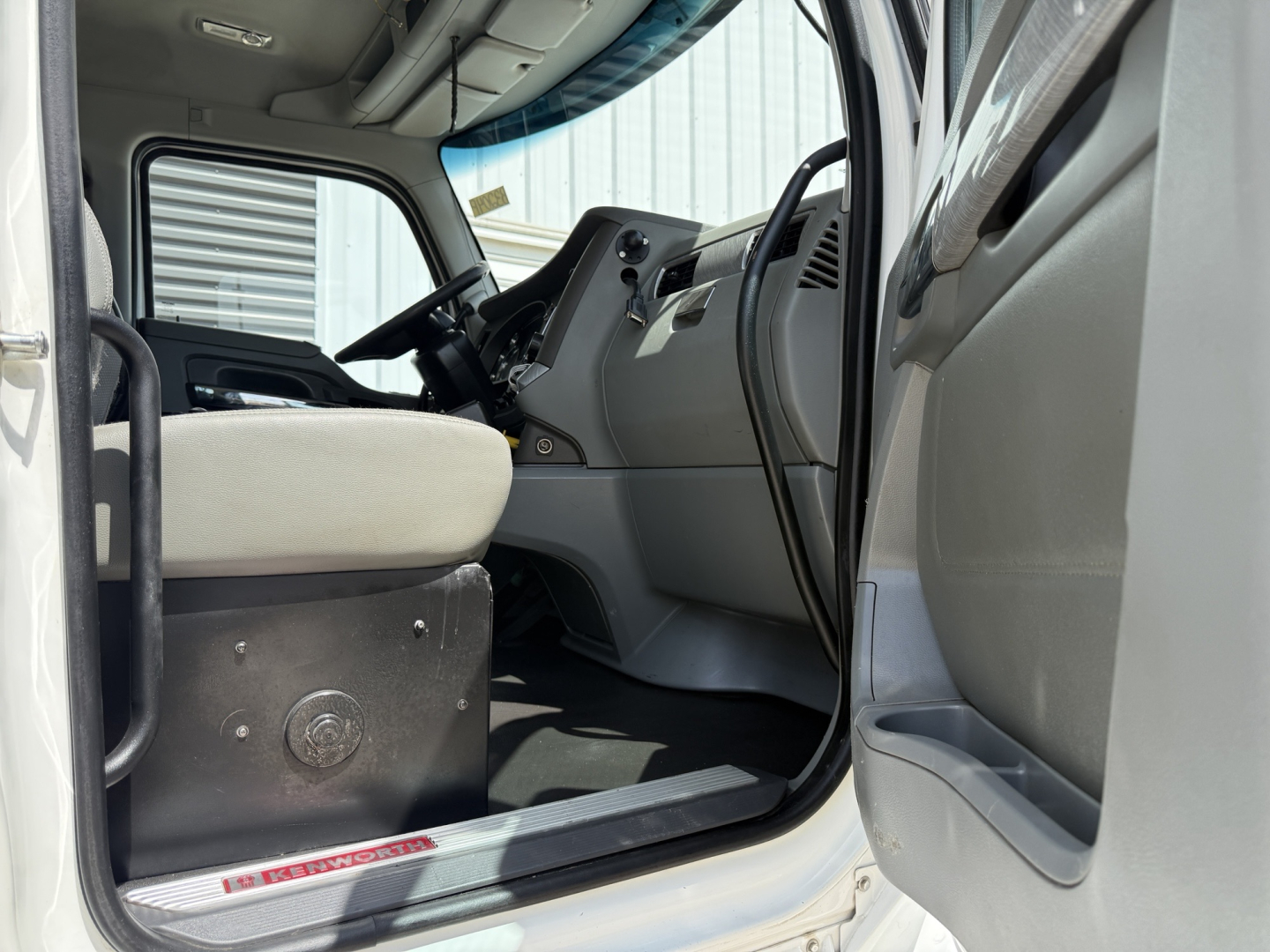 Kenworth T880 cab interior view from driver door opening showing steering wheel, dashboard, and seat.