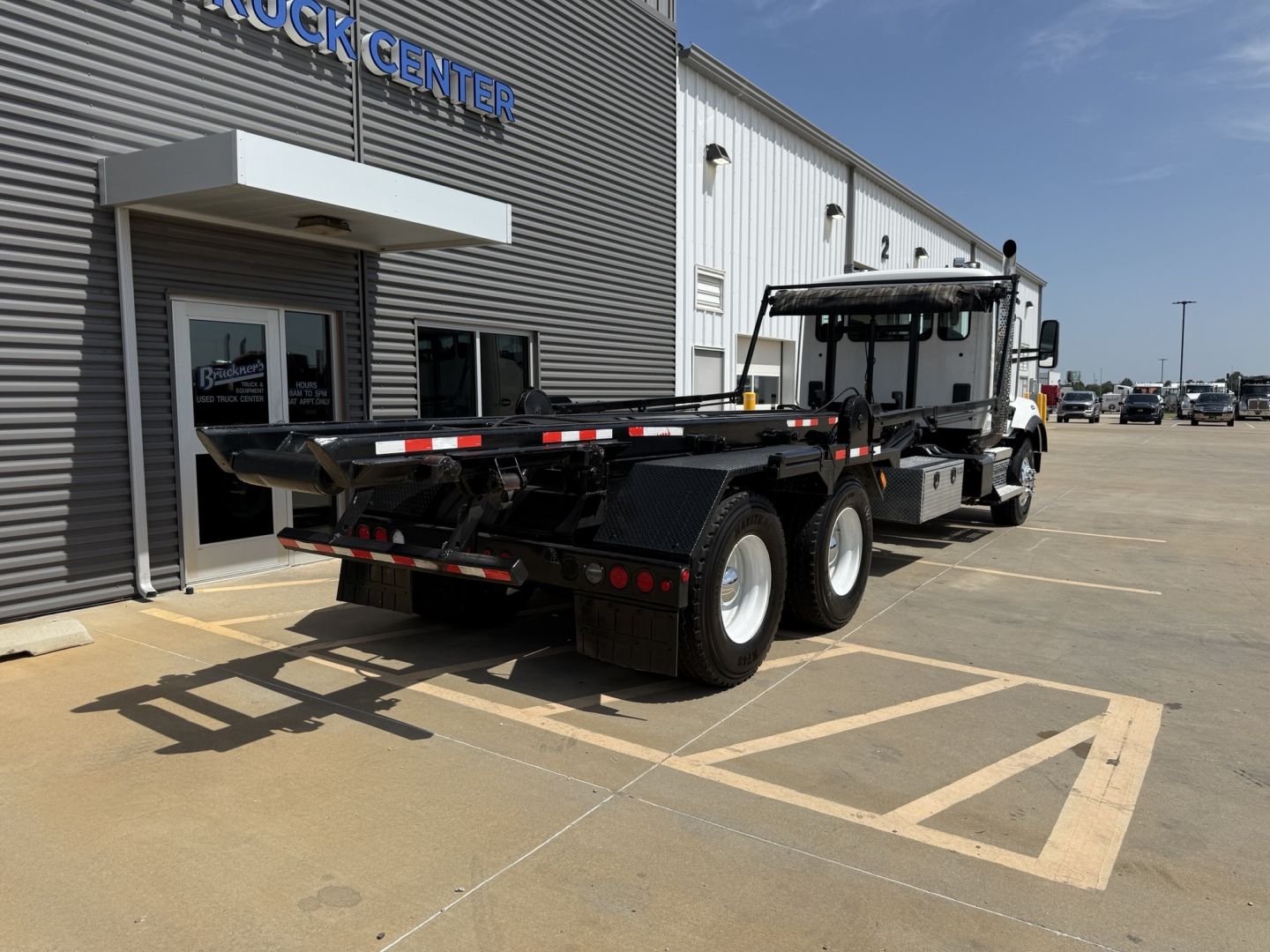 Kenworth T880 roll-off truck in a used vehicle lot, side and rear views showcasing flatbed and hydraulic system, VIN visible in listing, stock number B3205P.