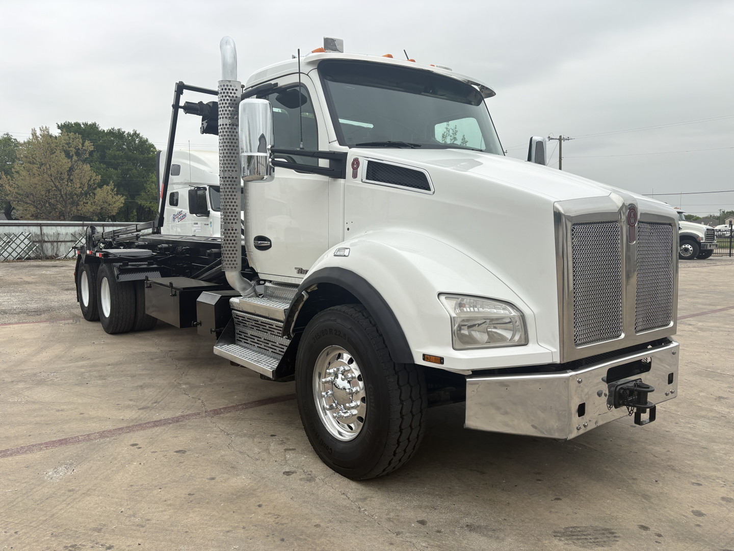Kenworth T880 roll-off truck in white, front-right view showing cab, chrome grille, tall exhaust stack, side steps, and rear chassis for wheel-lift bed.