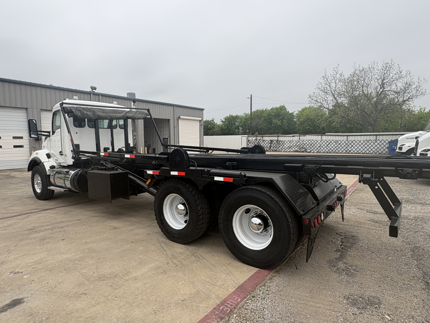 Kenworth T880 roll-off truck side view showing long flatbed with dual rear axles and wheel wells.