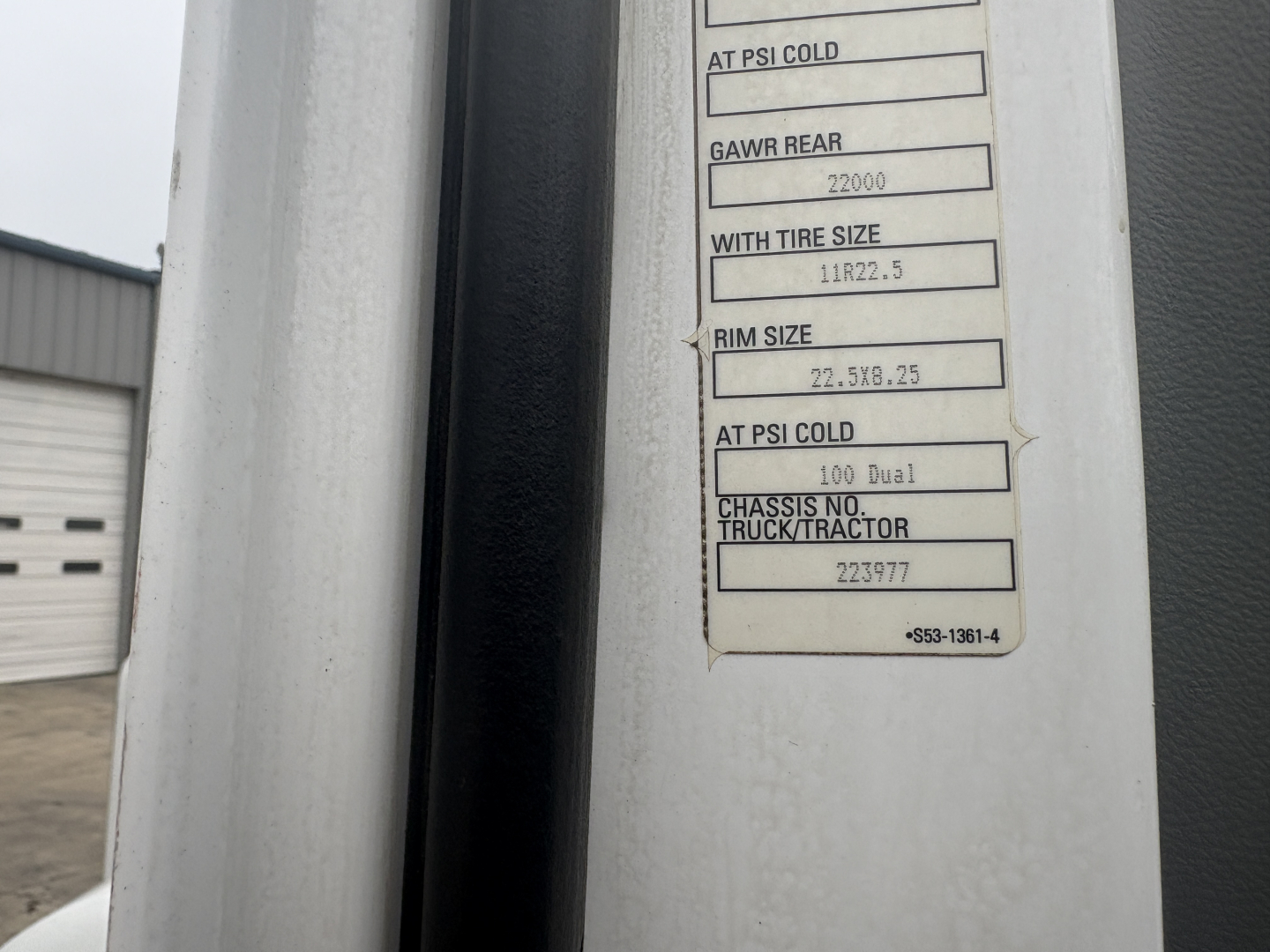 Label panel on Kenworth truck showing tire size and chassis data. Text includes 'GAWR REAR 22000', 'RIM SIZE 22.5J 8.25', 'WITH TIRE SIZE 11R22.5', 'CHASSIS NO. 223977' and other small lines.