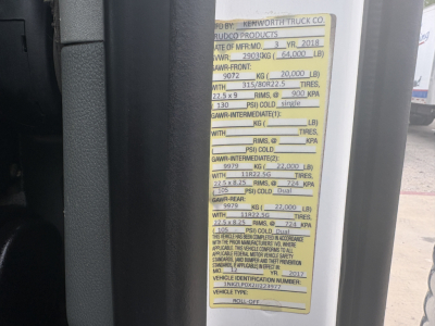 Vehicle identification sticker on Kenworth T880 roll-off truck showing axle weights and tires specifications.