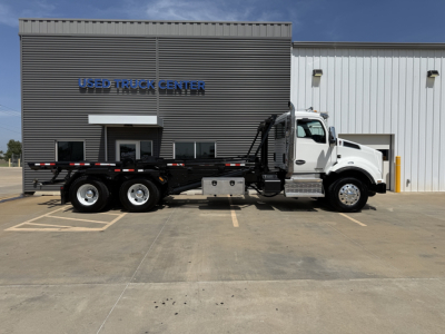 Kenworth T880 roll-off truck side view showing white cab and black flatbed with side rails, at a used truck center.