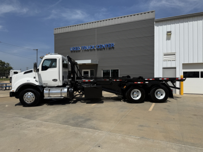 Kenworth T880 roll-off truck in front of dealership building with crane chassis and multiple axles.