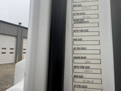 Kenworth T880 listing showing a door sticker with tire and rim specs, including GAWR rear 22000 and rim sizes, visible next to a light gray door frame.