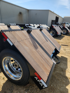 Trailer accessory showing wooden deck flip axles 102/54 with black metal frame and chrome wheel rims, Alpha branding on edge.