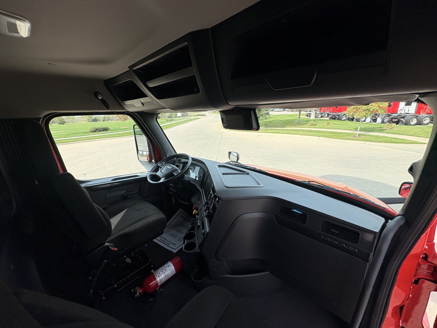 Cab interior of Freightliner PT126064S Daycab showing steering wheel, dashboard, center console, and passenger side; windshield with rear view mirror; fire extinguisher mounted under dash.