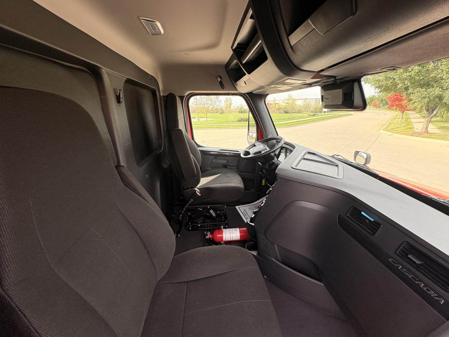 Cab interior of a Freightliner PT126064S T truck showing driver seat, passenger seat, steering wheel, dashboard, overhead compartments, and a fire extinguisher near the floor; windshield and side window view.