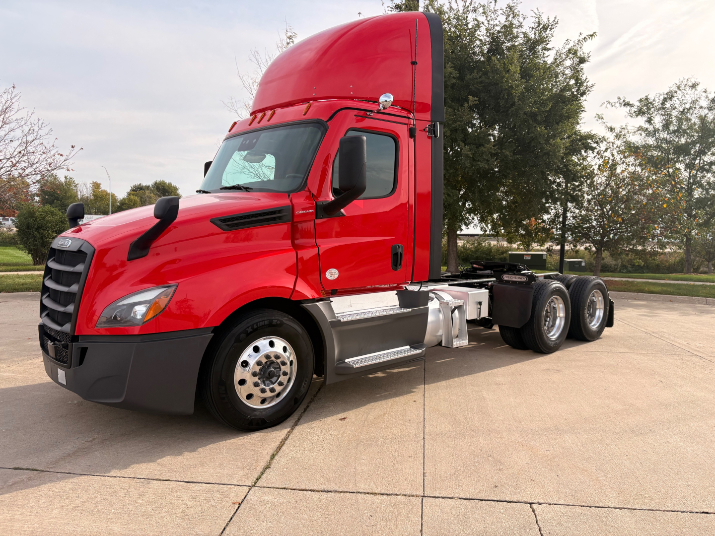 Red Freightliner semi truck cab in a parking lot, with empty sleeper and chassis visible, no text readable on the cab or decals.