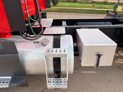 Truck fuel tank area and aluminum toolbox on a Freightliner day cab chassis with steps and wiring visible.