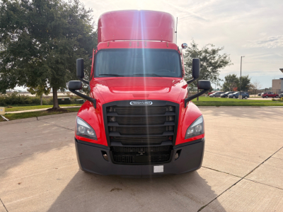 Freightliner truck cab front view showing bold black grille, red hood and sleeper, large side mirrors, daytime running lights, and front bumper.