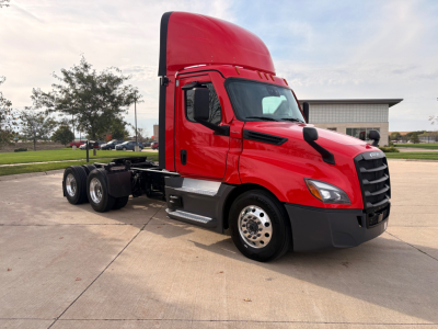 Freightliner PT126064S T conventional daycab truck side view showing red cab and chassis, dual rear axles, aerodynamic mirrors, and large front grille.
