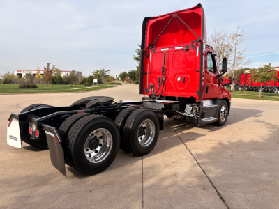 Truck chassis with red cab and rear dual axles, side view showing fifth wheel and exposed drivetrain components.