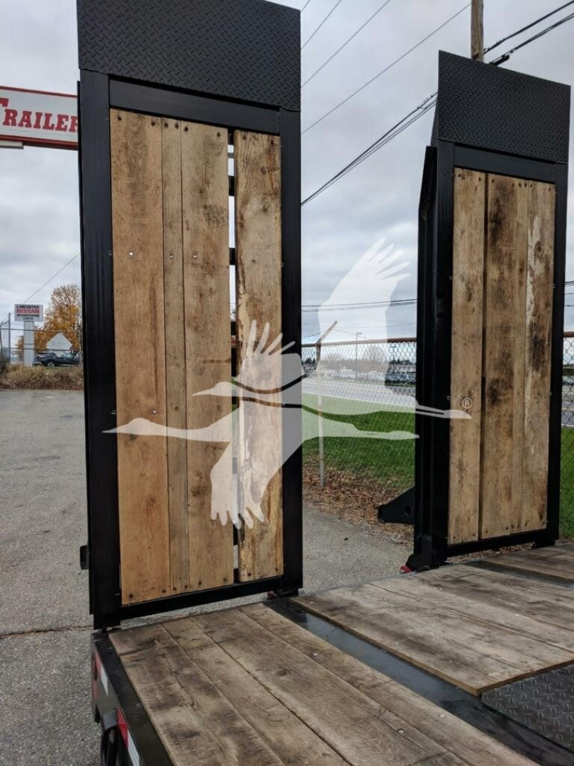 Trailer components showing two tall wooden ramp doors with black metal frames on a flatbed trailer, with a distant sign reading ‘trailer’ and power lines in overcast sky.