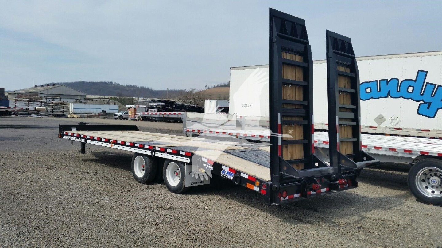 Trailer flatbed dual-axle with loading ramps in a yard, with a white truck trailer in background.