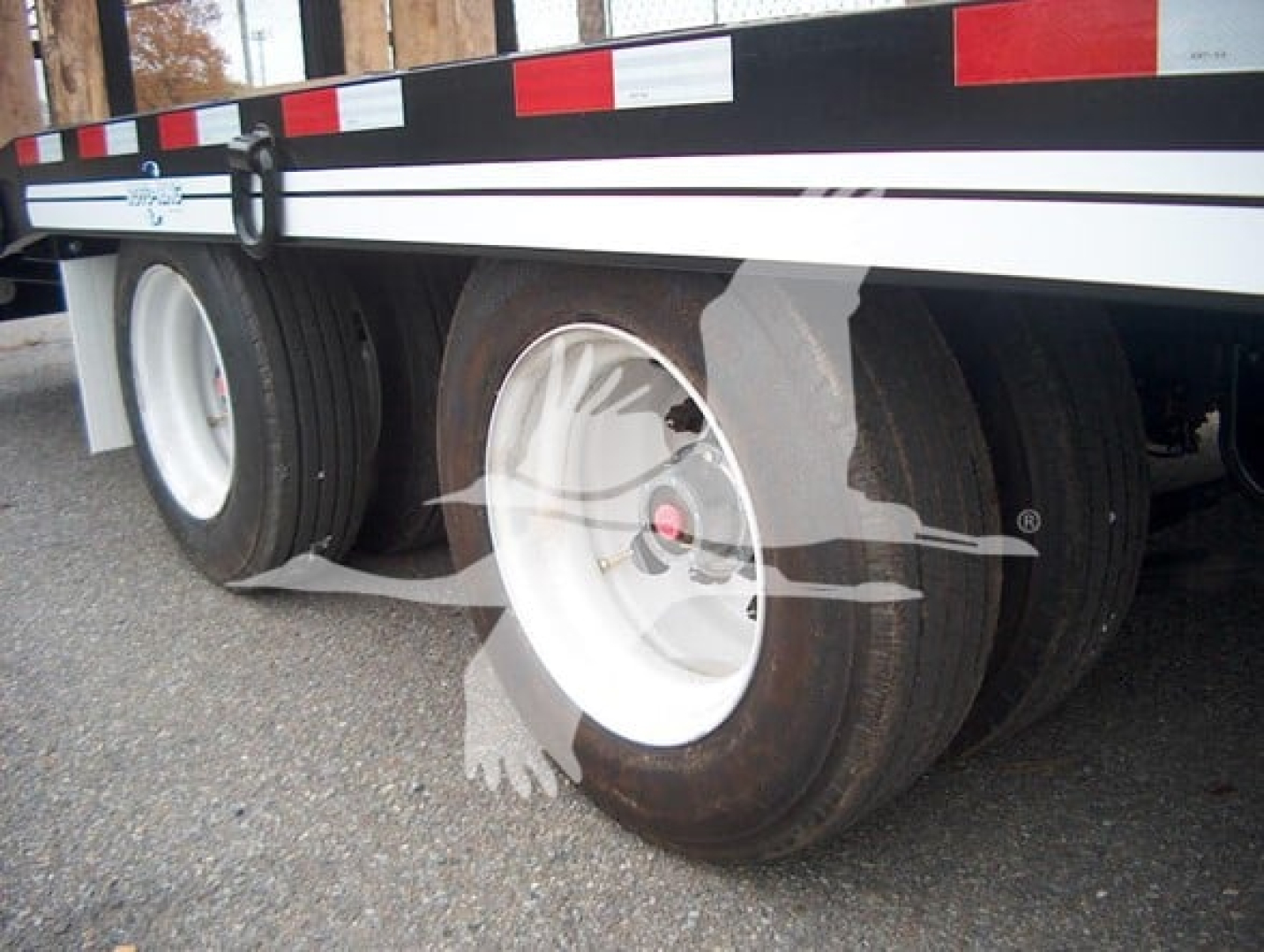 Trailer wheel assembly showing dual tires on a flatbed trailer with white rims and black tires.