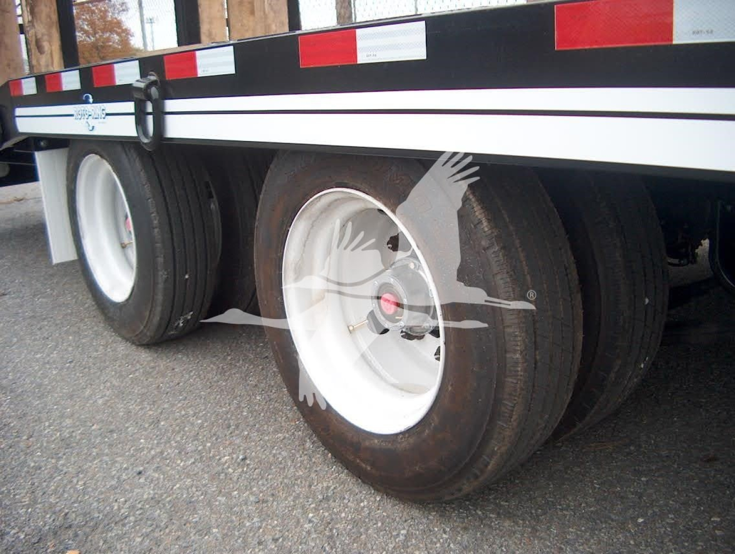 Trailer wheel assembly with dual rear tires and white rims; side rail and reflective tape visible.