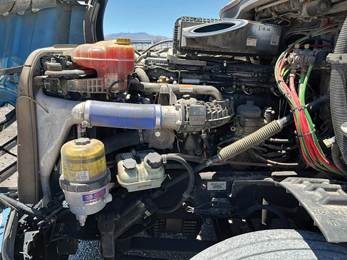 Truck engine bay of a 2021 Freightliner Cascadia126 showing coolant reservoir, oil filter, hoses, wiring, and air intake.
