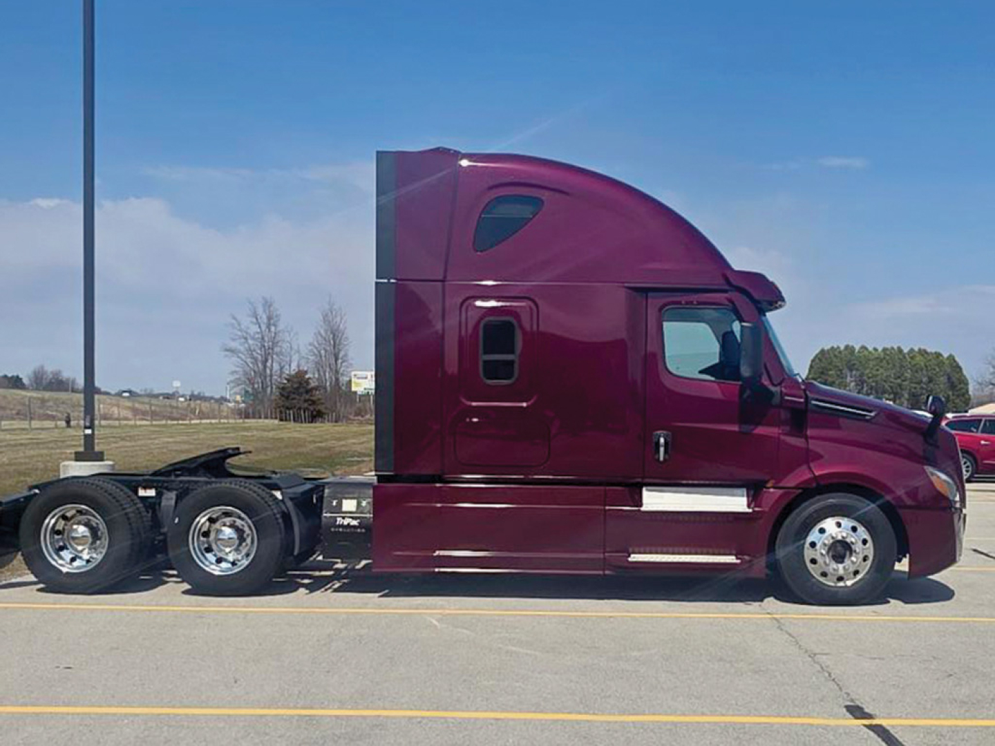 Side view of a maroon Freightliner Cascadia 126 semi-truck tractor, showing cab with sleeper, tandem rear axles, chrome wheels, and exhaust area.