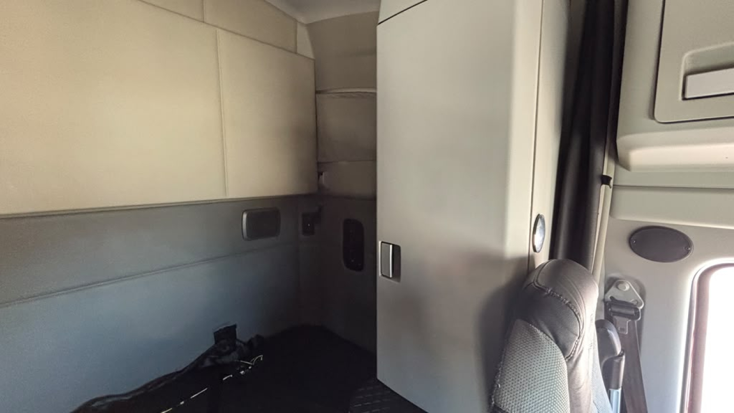 Kenworth T680 cab interior showing sleeper area and doorway with paneling and storage cabinet.