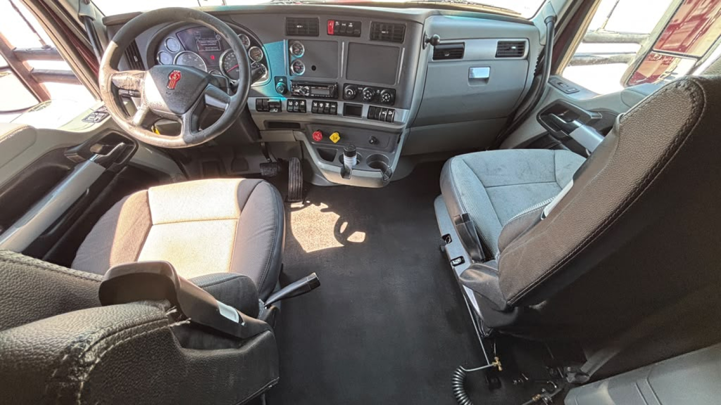 Kenworth T680 truck cockpit showing steering wheel and dashboard with controls and two front seats.