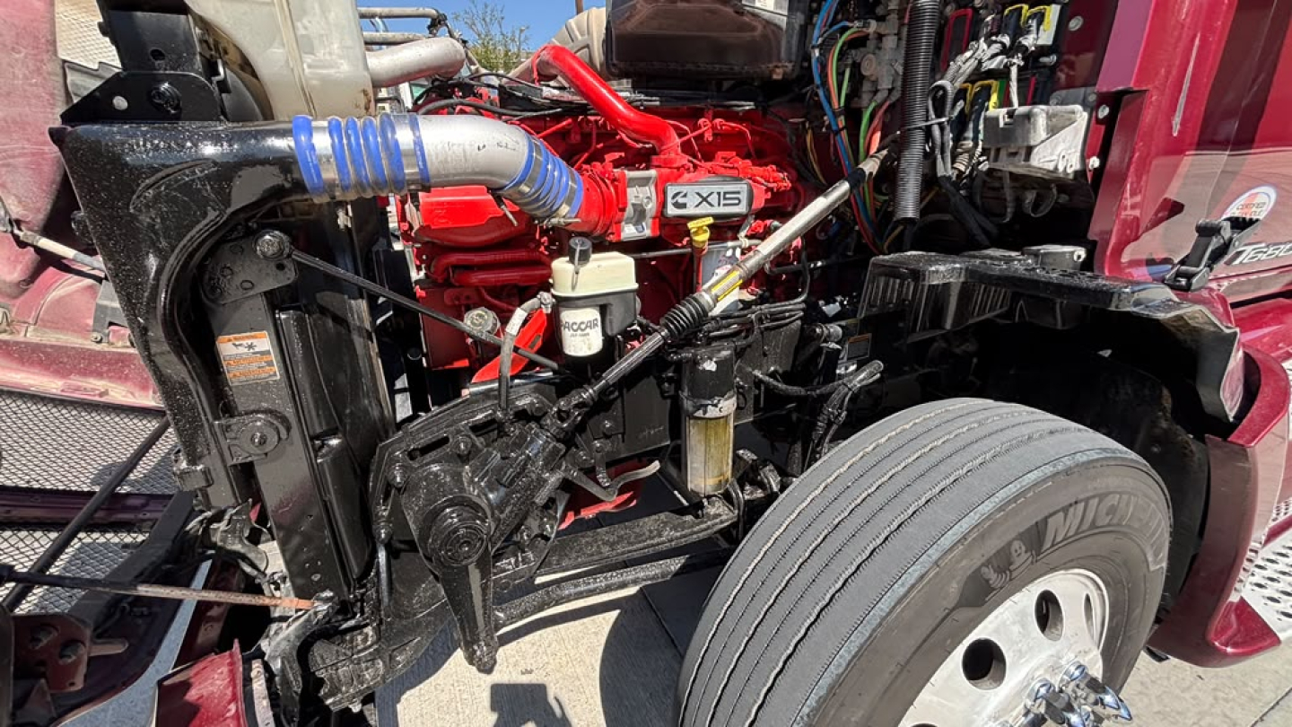 Kenworth T680 engine bay showing red engine with X15 badge and surrounding hoses and components.